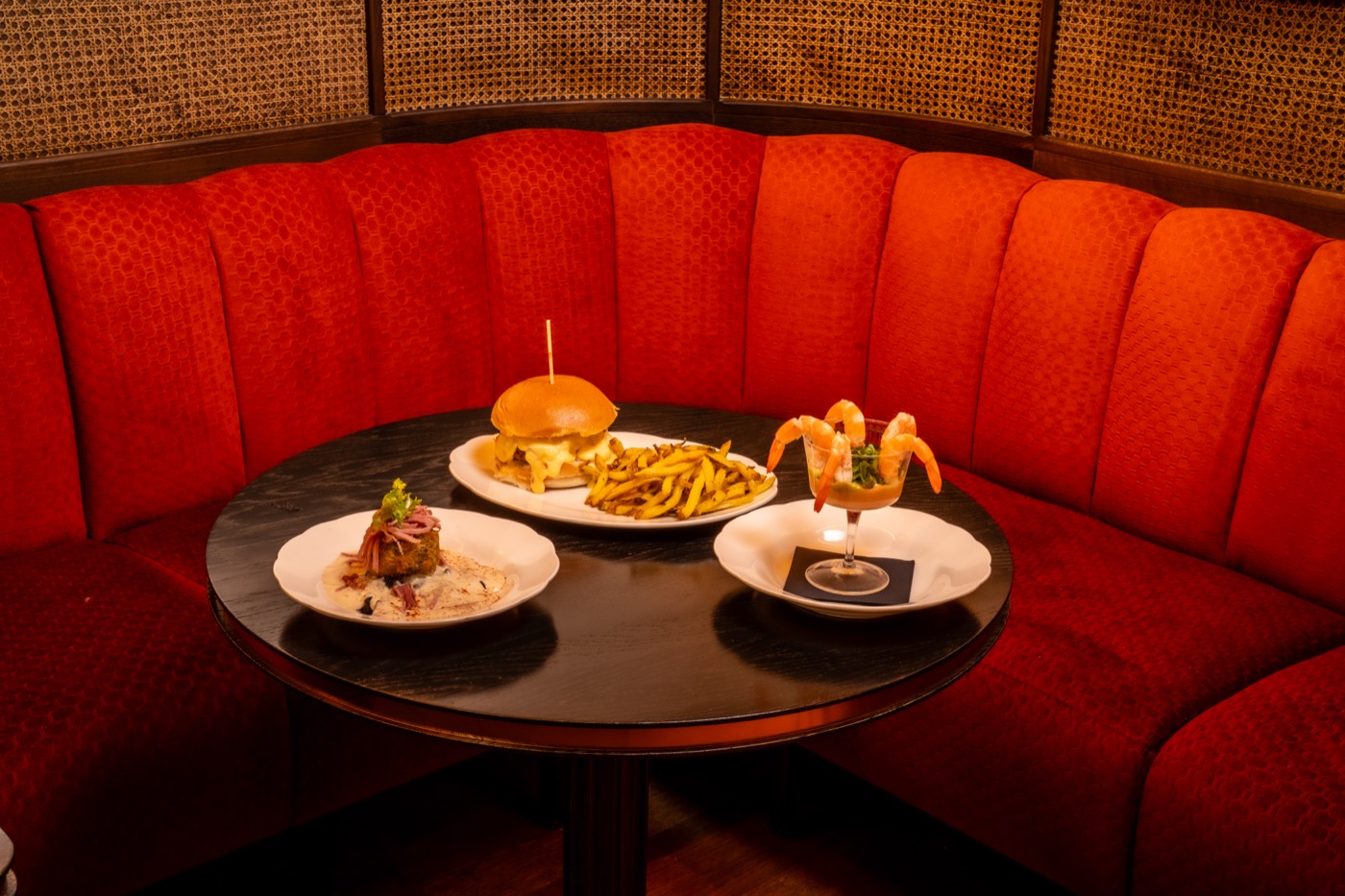 Banquette rouge en arc, burger et cocktail de crevettes sur table ronde
