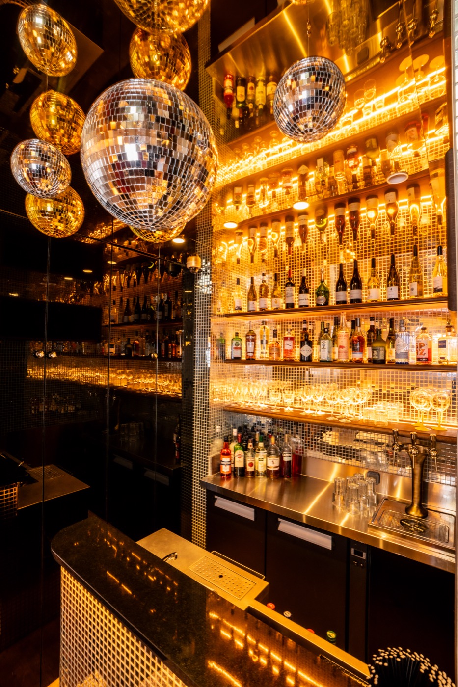 L’Émeraude, le bar des Causeurs, mur de bouteilles rétroéclairé sous les boules à facettes